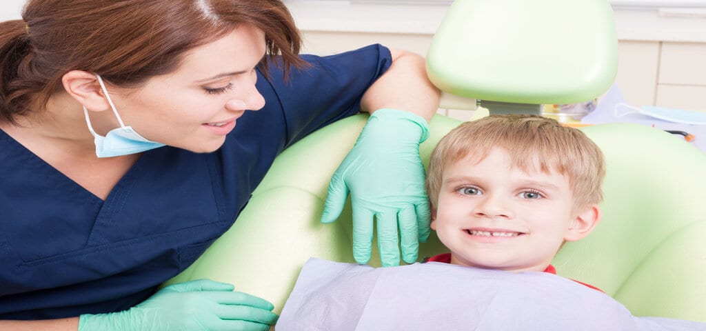 Zahnmedizinische Fachangestellte beugt sich über einen lächelnden Jungen im Behandlungsstuhl